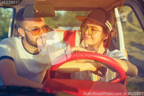 Image of Laughing romantic couple sitting in car while out on a road trip at summer day