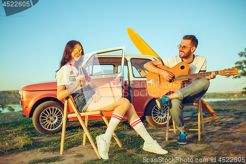 Image of Couple sitting and resting on the beach playing guitar on a summer day near river