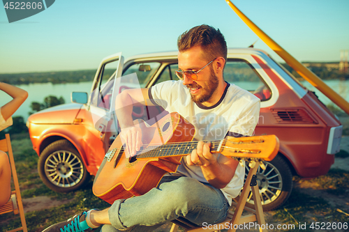 Image of Couple sitting and resting on the beach playing guitar on a summer day near river