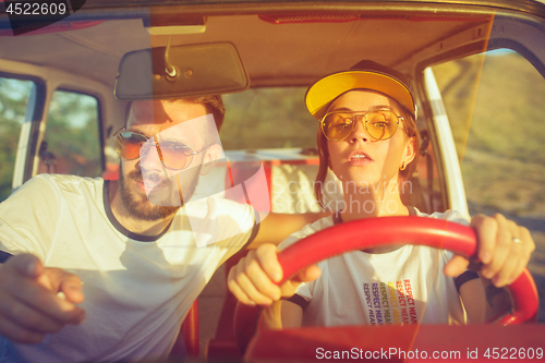 Image of Laughing romantic couple sitting in car while out on a road trip at summer day