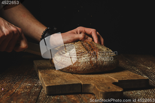 Image of Hands of a young man cut fresh rye bread