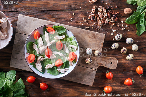 Image of A plate of salad from boiled meat, quail eggs, spinach and tomatoes on a wooden board on the kitchen table. Dietary snack Flat lay