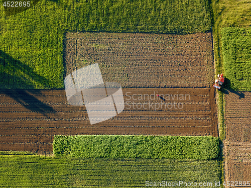 Image of Aerial view from the drone, a bird\'s eye view of agricultural fields with a road through and a tractor on it in the spring evening at sunset