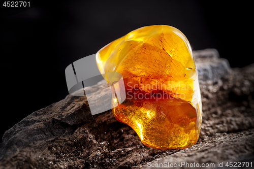 Image of Natural amber. A piece of yellow opaque natural amber on large piece of dark stoned wood.