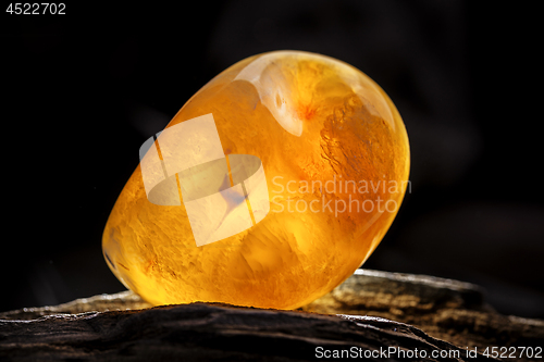 Image of Natural amber. A piece of yellow opaque natural amber on large piece of dark stoned wood.