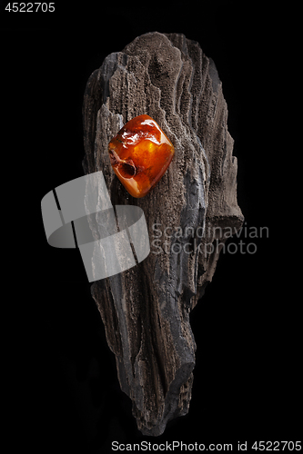 Image of Natural amber. A piece of yellow and red semi transparent natural amber on piece of stoned wood.