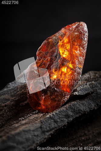 Image of Natural amber. A piece of yellow and red semi transparent natural amber on piece of stoned wood.