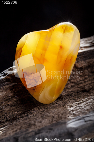 Image of Natural amber. A piece of yellow opaque natural amber on large piece of dark stoned wood.