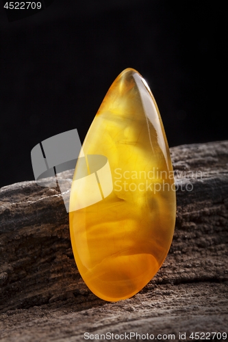 Image of Natural amber. A piece of yellow opaque natural amber on large piece of dark stoned wood.