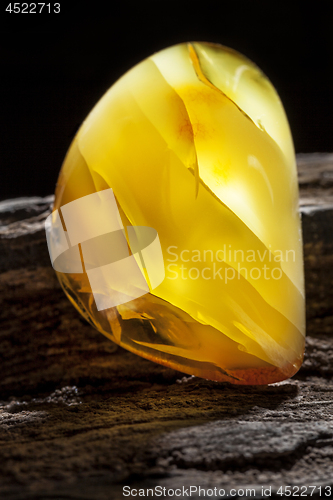 Image of Natural amber. A piece of yellow opaque natural amber on large piece of dark stoned wood.