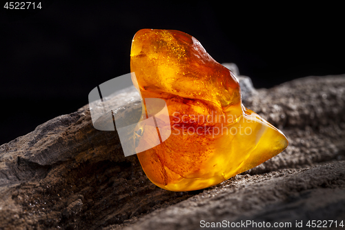 Image of Natural amber. A piece of yellow and red semi transparent natural amber on piece of stoned wood.