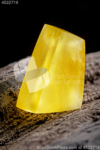 Image of Natural amber. A piece of yellow opaque natural amber on large piece of dark stoned wood.