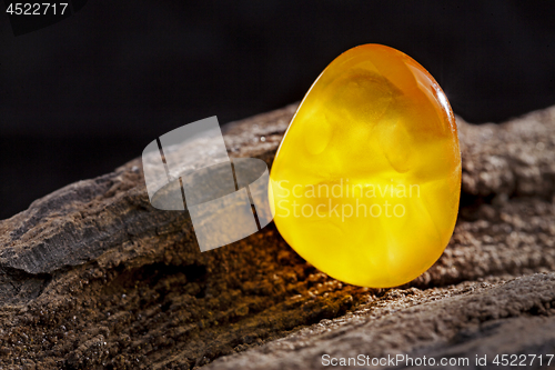 Image of Natural amber. A piece of yellow opaque natural amber on large piece of dark stoned wood.