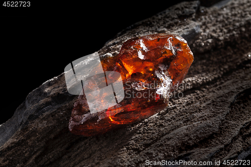 Image of Natural amber. A piece of yellow and red semi transparent natural amber on piece of stoned wood.