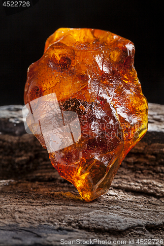 Image of Natural amber. A piece of yellow and red semi transparent natural amber on piece of stoned wood.