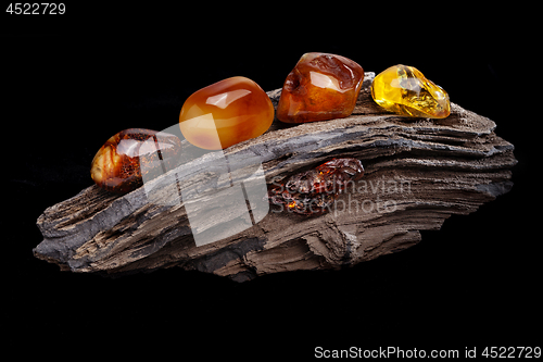 Image of Natural amber. Several pieces of different colors of natural amber on large piece of stoned wood.