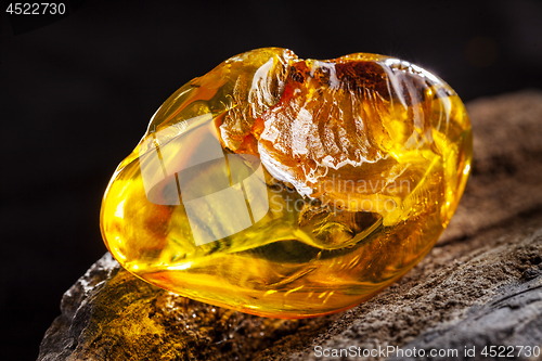 Image of Natural amber. A piece of yellow transparent natural amber on large piece of dark stoned wood.