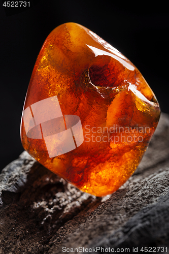 Image of Natural amber. A piece of yellow and red semi transparent natural amber on piece of stoned wood.