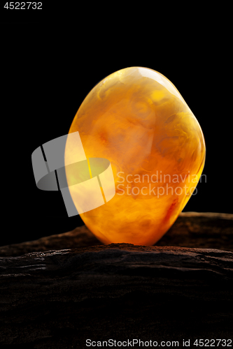 Image of Natural amber. A piece of yellow opaque natural amber on large piece of dark stoned wood.