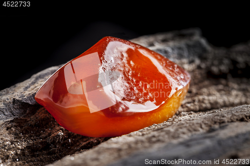 Image of Natural amber. A piece of yellow and red semi transparent natural amber on piece of stoned wood.