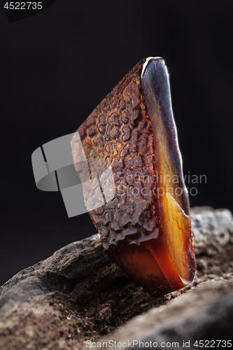 Image of Natural amber. A piece of dark red semi transparent natural amber on piece of stoned wood.
