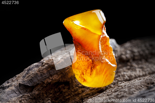 Image of Natural amber. A piece of yellow opaque natural amber on large piece of dark stoned wood.