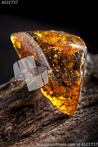 Image of Natural amber stone. A piece of dirty transparent yellow amber on piece of stoned wood.