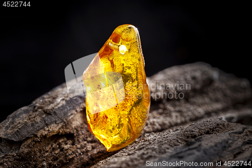 Image of Natural amber. A piece of yellow transparent natural amber on large piece of dark stoned wood.