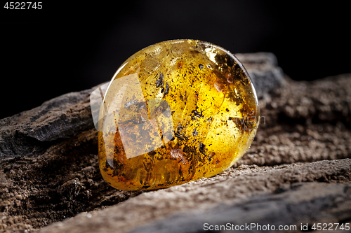 Image of Natural amber stone. A piece of dirty transparent yellow amber on piece of stoned wood.