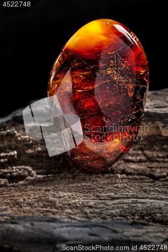 Image of Natural amber. A piece of dark red semi transparent natural amber on piece of stoned wood.