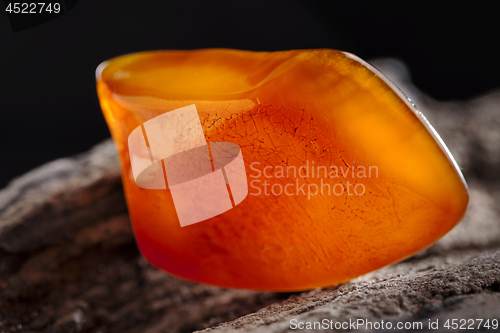 Image of Natural amber. A piece of yellow and red semi transparent natural amber on piece of stoned wood.