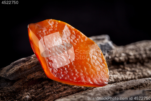 Image of Natural amber. A piece of yellow and red semi transparent natural amber on piece of stoned wood.