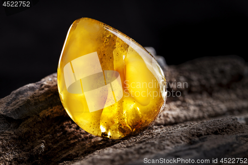 Image of Natural amber. A piece of yellow opaque natural amber on large piece of dark stoned wood.