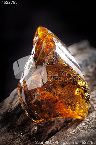 Image of Natural amber stone. A piece of dirty transparent yellow amber on piece of stoned wood.