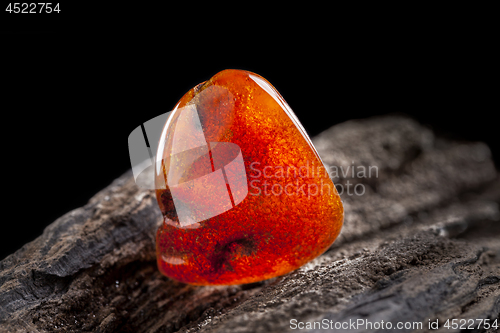 Image of Natural amber. A piece of yellow and red semi transparent natural amber on piece of stoned wood.