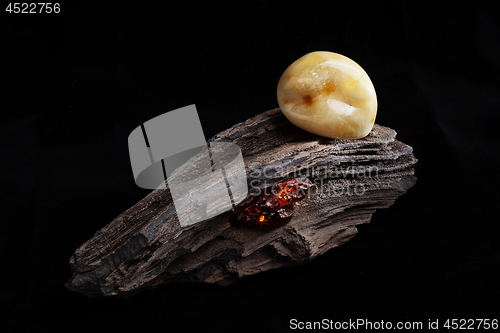 Image of Natural amber. A piece of yellow opaque natural amber on large piece of dark stoned wood.