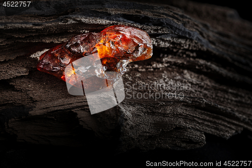 Image of Natural amber. A piece of yellow and red semi transparent natural amber on piece of stoned wood.