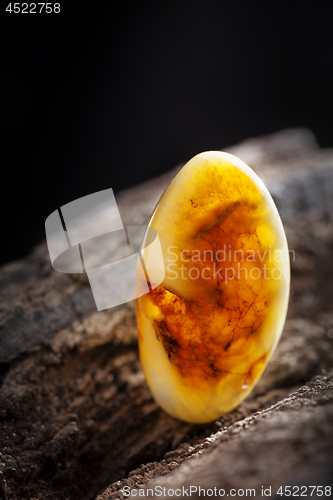 Image of Natural amber. A piece of yellow opaque natural amber on large piece of dark stoned wood.