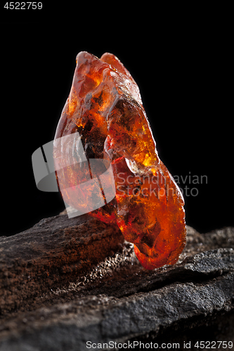 Image of Natural amber. A piece of yellow and red semi transparent natural amber on piece of stoned wood.