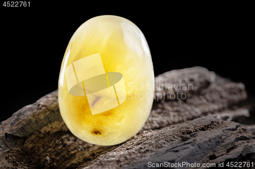 Image of Natural amber. A piece of yellow opaque natural amber on large piece of dark stoned wood.