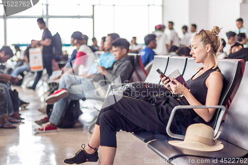 Image of Female traveler using her cell phone while waiting to board a plane at departure gates at asian airport terminal.