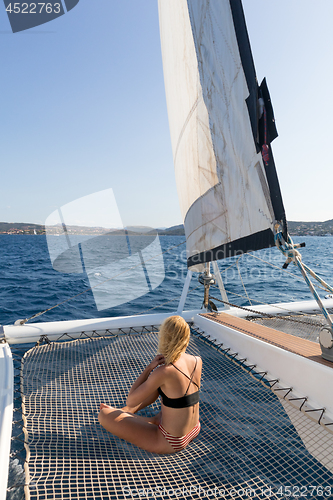 Image of Beautiful woman relaxing on a summer sailing cruise, sitting and sunbathing in hammock of luxury catamaran sailing around Maddalena Archipelago, Sardinia, Italy in warm afternoon light