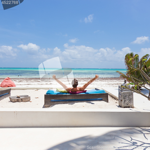 Image of Relaxed man in luxury lounger, arms rised, enjoying summer vacations on beautiful beach.