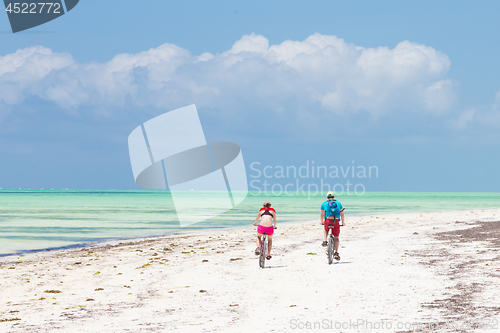 Image of Two caucasian tourist cycling on perfect tropical white sandy Paje beach, Zanzibar, Tanzania.