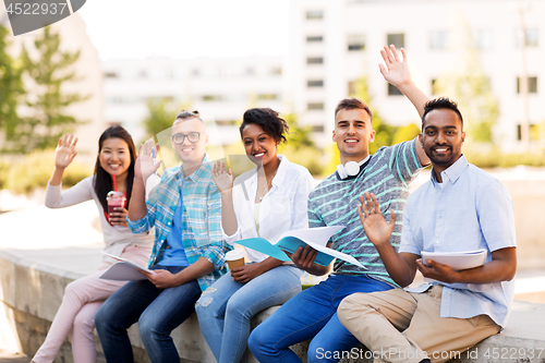 Image of students with notebook waving hands outdoors