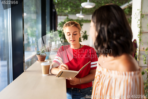 Image of woman with friend at cafe writing to notebook