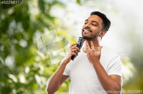 Image of smiling indian man shaving beard with trimmer