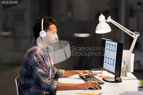 Image of creative man in headphones working at night office