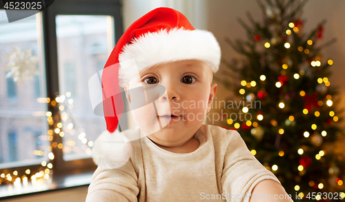 Image of baby boy in santa hat taking selfie on christmas