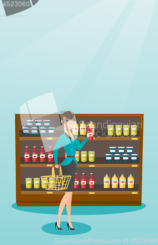 Image of Woman holding shopping basket and bottle of sauce.